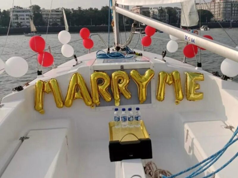 Man down on one knee proposing to woman on a luxurious yacht, sparkling ocean in the background.